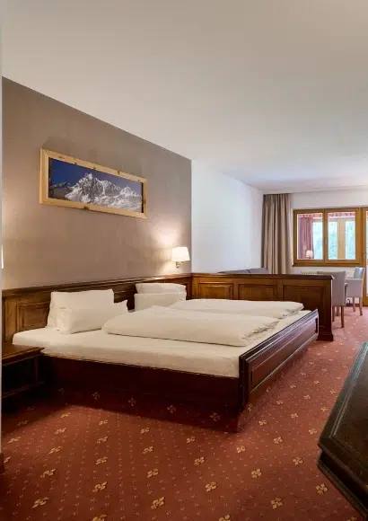 Kaunertaler Familienzimmer mit Doppelbett, Holzmöbeln, Teppichboden und verdunkeltem Fenster.