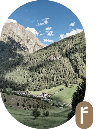 Ein kleines Dorf, eingebettet in ein grünes Tal mit Bergen und blauem Himmel im Hintergrund.