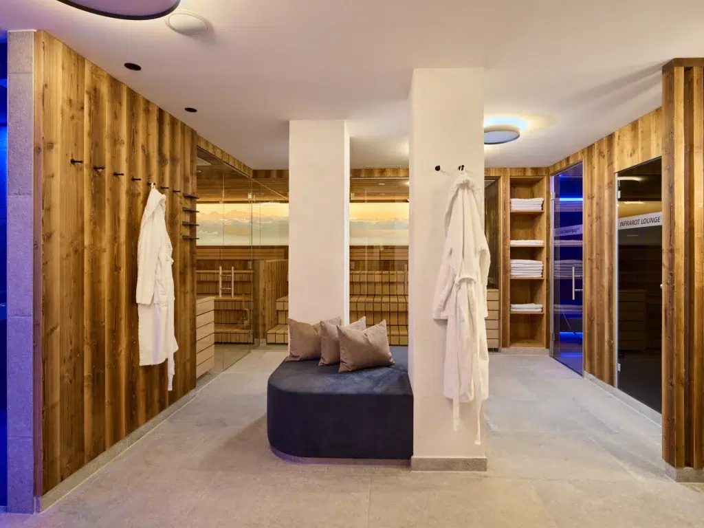 Moderne Umkleidekabine des Hotel Kaunertal Spa mit Bademänteln, Holzwänden, Handtüchern und einer gepolsterten Bank.