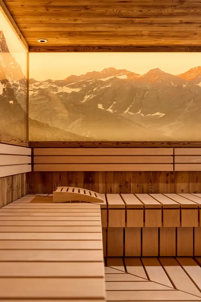 Moderne Holzsauna im Hotel Kaunertal, mit einem großen Fenster, das den Blick auf den Sonnenuntergang in den Bergen freigibt.