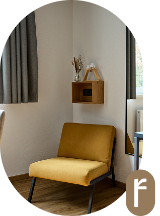 Gelber Stuhl neben einem Wandregal und einem Fenster mit grauen Vorhängen in einem gemütlichen Zimmer.