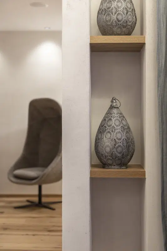 Dekorative Vasen auf Holzregalen neben einem modernen grauen Stuhl in einem Wellnesshotel Kaunertal.