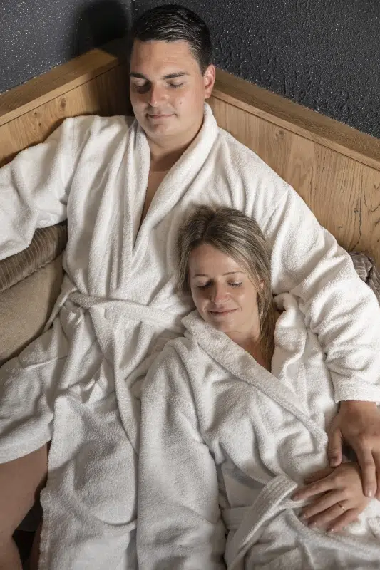 Ein Paar in weißen Gewändern entspannt sich im Wellnesshotel Kaunertal und lächelt mit geschlossenen Augen.