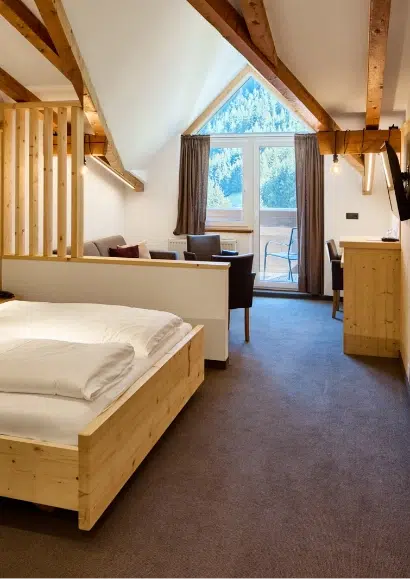 Modernes Kaunertaler Familienzimmer mit Holzbalken, Bett, Sitzecke und Balkon mit Bergblick.