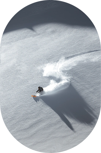 Ein Snowboarder carvt durch frischen Kaunertaler Pulverschnee auf einer sonnigen Piste, die einen langen Schatten wirft.