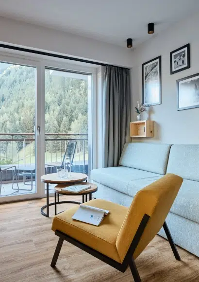 Modernes Wohnzimmer mit gelbem Sessel, Sofa und Kaunertaler Familienzimmer Balkon mit Blick auf Bäume.