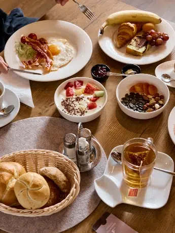 Frühstückstisch mit Eiern, Speck, Gebäck, Obst, Nüssen, Brot, Tee und Kaffee.