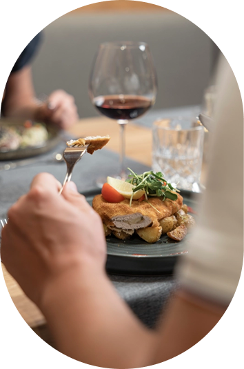 Eine Person genießt Kulinarik: eine Gabel voll Essen, Huhn und Gemüse, mit Rotwein daneben.