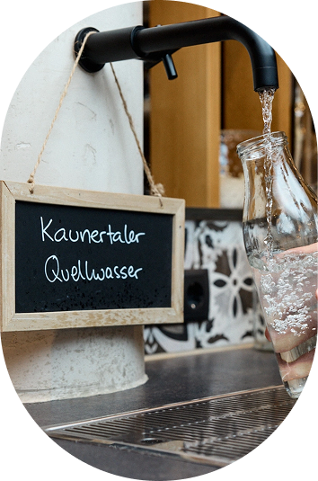 Eine Glasflasche wird an einer Kaunertaler Quellwasser-Zapfstelle mit Wasser nachhaltig urlaub gefüllt.