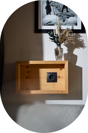 Hölzernes Wandregal in einer gemütlichen Kaunertaler Unterkunft mit Vase, Steckdose und gerahmtem Foto darüber.