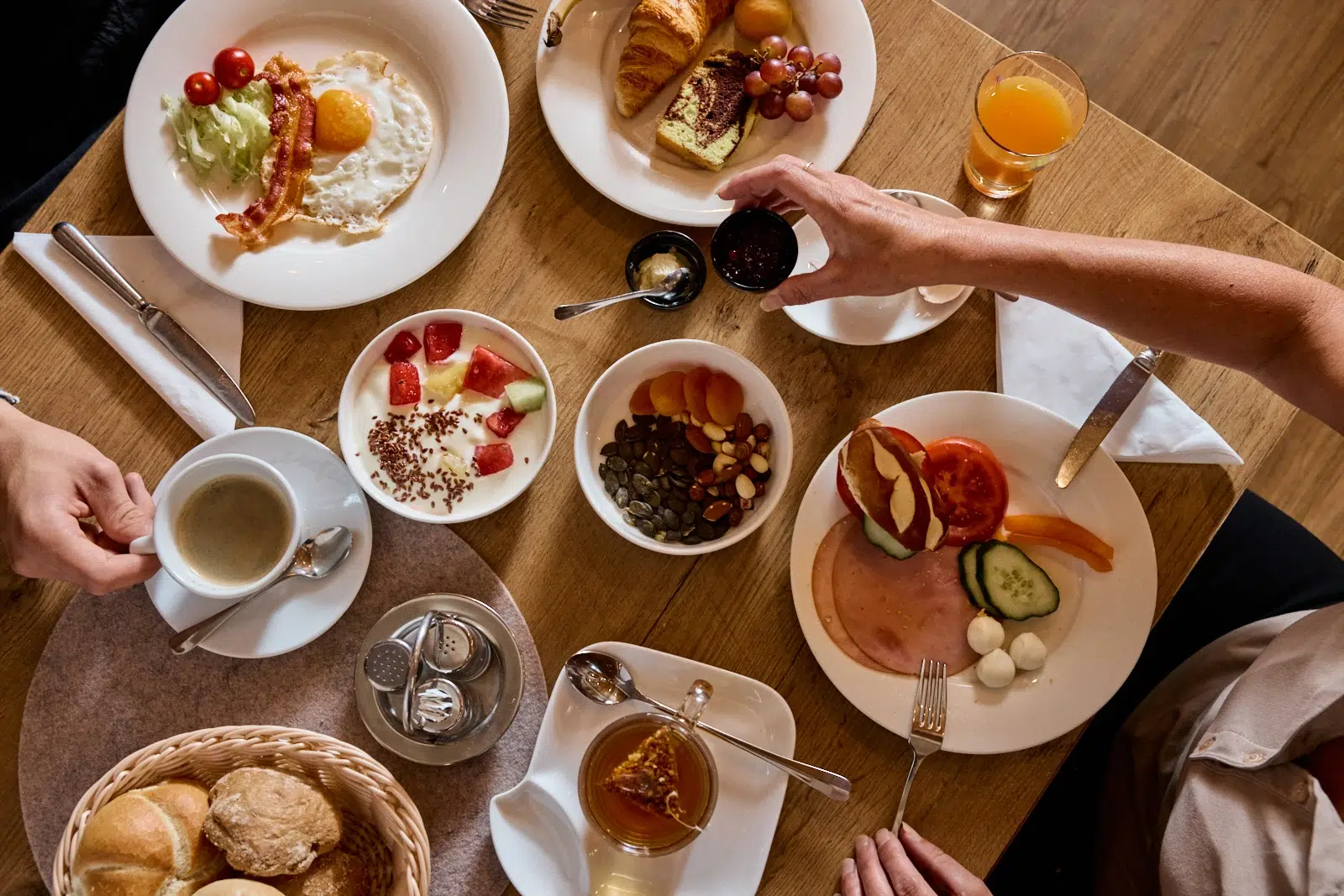 Ein Frühstückstisch im Hotel Kaunertal mit Eiern, Obst, Gebäck, Kaffee und Gästen, die nach dem Essen greifen.