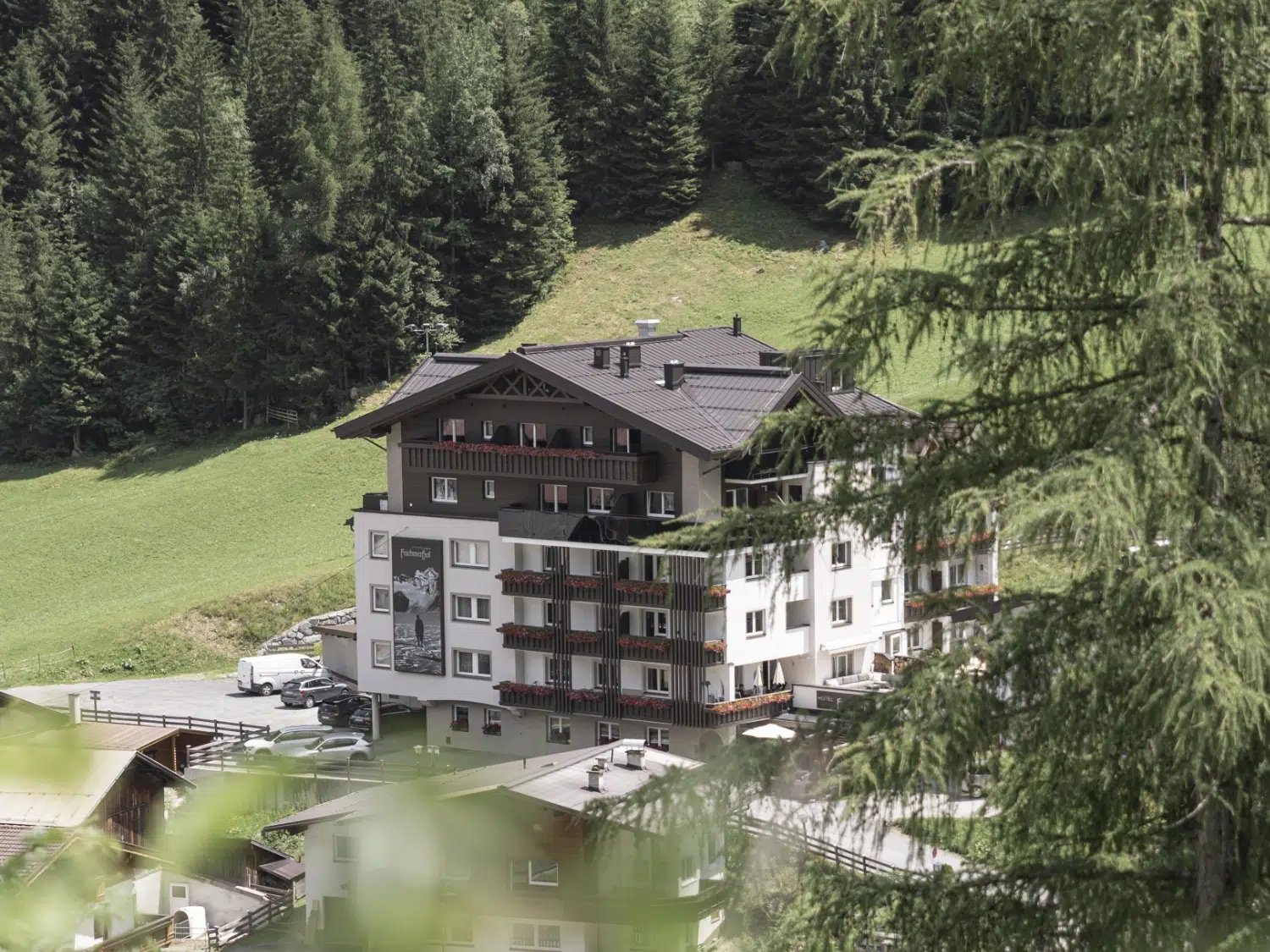 Das Berghotel Feichtnerhof Kaunertal inmitten von Zirbenbäumen und Grünflächen an einem sonnigen Tag.