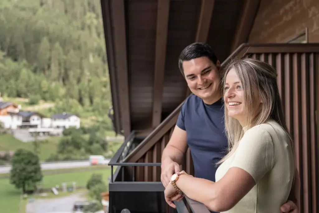 Lächelndes Pärchen auf einem Balkon, das die Aussicht genießt - Kaunertal Urlaub buchen für Erinnerungen.