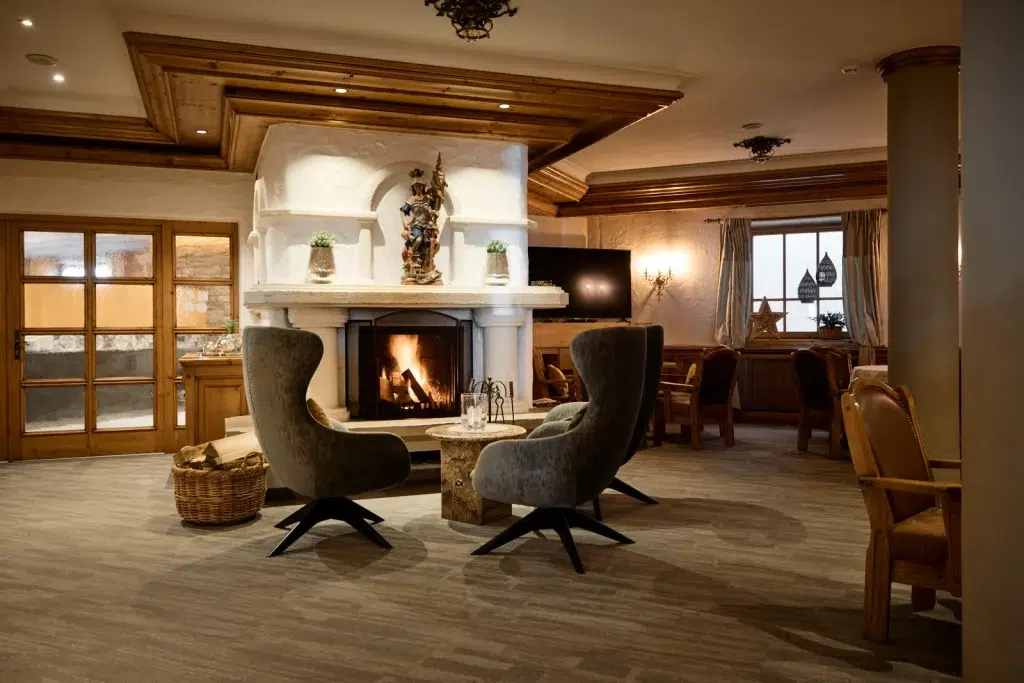 Gemütliche Lounge im Feichtnerhof Kaunertal mit Sesseln, beleuchtetem Kamin, rustikaler Einrichtung und warmer Beleuchtung.