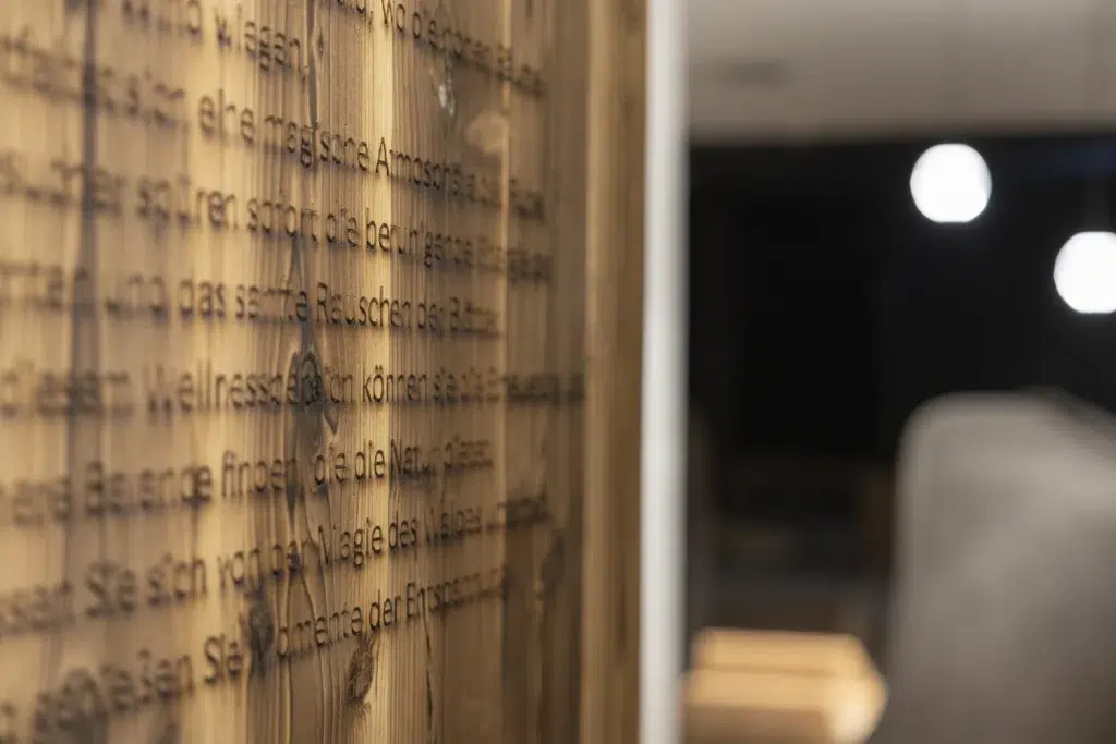 In eine Holzwand geätzter Text im Wellnesshotel Kaunertal, mit verschwommenen Sofas und runden Leuchten.
