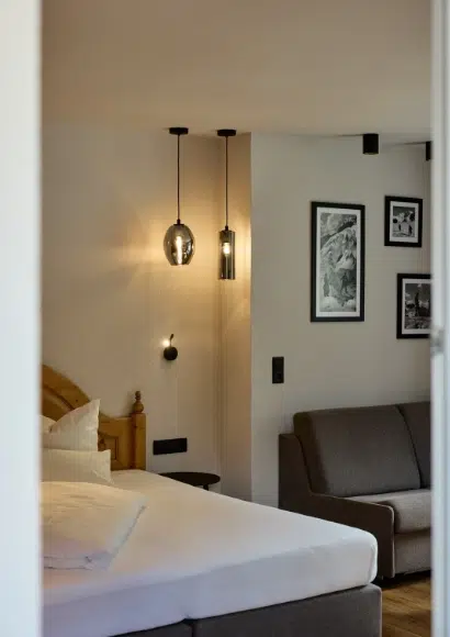 Modernes Kaunertal Doppelzimmer mit Hängeleuchten, gerahmter Wandkunst, Bett und grauem Sofa.