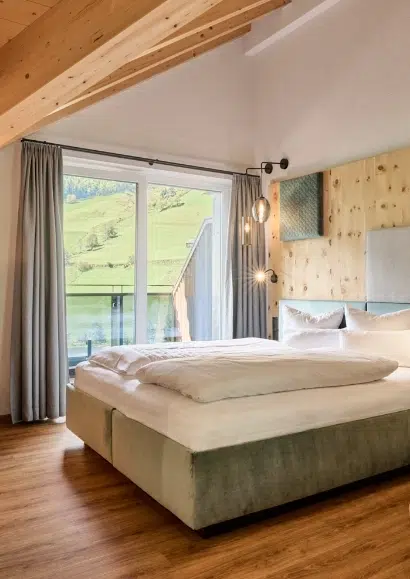 Modernes Kaunertaler Doppelzimmer mit großem Bett, Holzakzenten und Balkon mit Blick auf grüne Hügel.