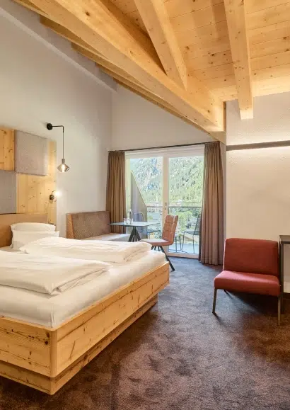 Gemütliches Kaunertaler Familienzimmer mit Holzdecke, Bett, Tisch, Stühlen und Fenster mit Bergblick.
