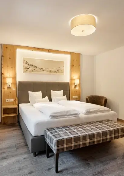 Modernes Kaunertaler Doppelzimmer mit Doppelbett, karierter Bank und warmer Beleuchtung.