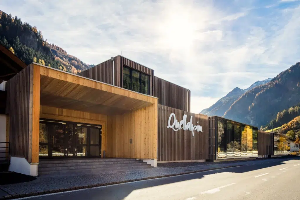 Modernes Holzhotel Kaunertal mit großen Glasfenstern, Berge im Hintergrund, sonniger Himmel.