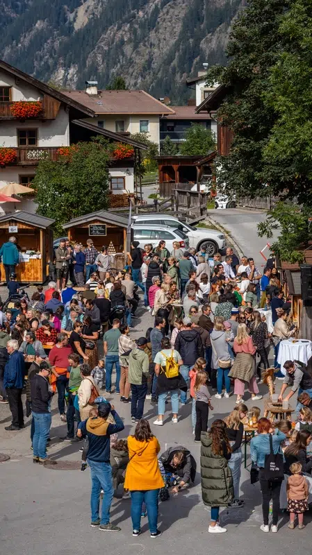Bei Veranstaltungen Kaunertal versammelt sich eine große Menschenmenge auf einem lebhaften Straßenmarkt in einem Bergdorf.