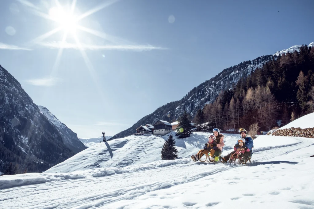 Schlittenfahrer auf einer verschneiten Kaunertaler Winterpiste mit Bergen im Hintergrund.