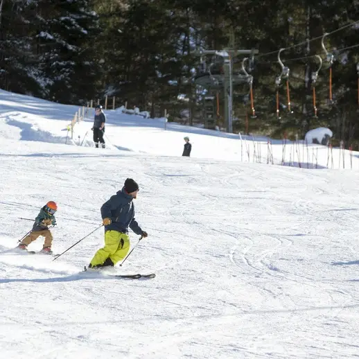 Erwachsene und Kinder beim Skifahren auf einer verschneiten Piste in der Nähe des Hotels Kaunertal, mit Bäumen und einem Skilift dahinter.