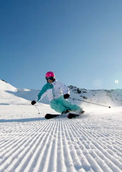 Ein Skifahrer in farbenfroher Ausrüstung fährt an einem sonnigen Tag einen verschneiten Hang mit einem Kaunertaler Skipass hinunter.