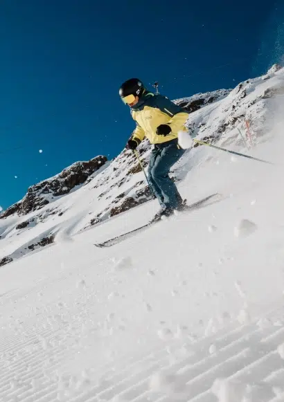 Person beim Skifahren auf einer verschneiten Piste mit Kaunertaler Skipass unter strahlend blauem Himmel.
