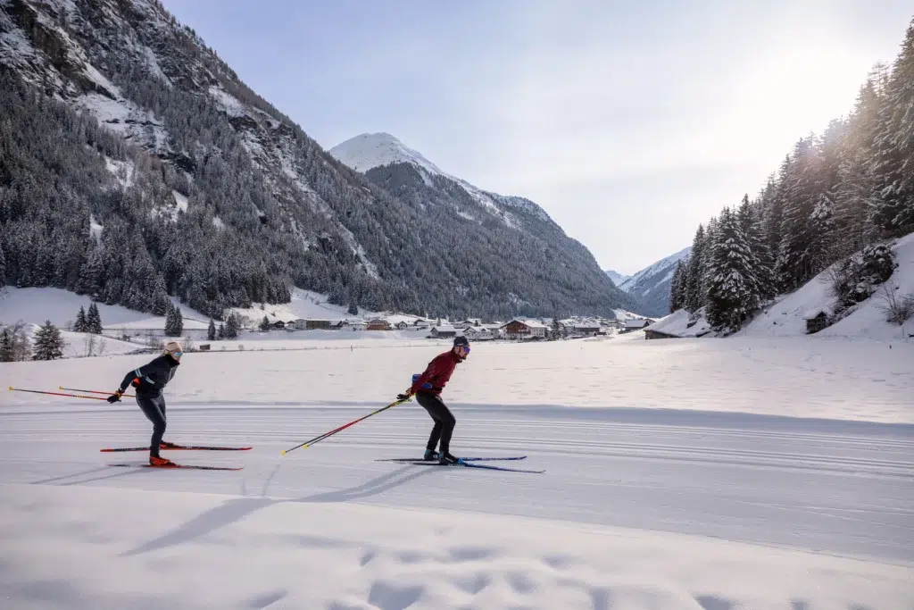 Zwei Personen beim Skilanglauf auf einer verschneiten Winter-Kaunertaler Loipe in einer Berglandschaft.