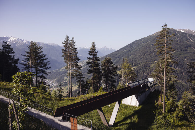 Berglandschaft mit Bäumen und einer modernen Kaunertaler Sommer-Aussichtsplattform über dem Berghang.