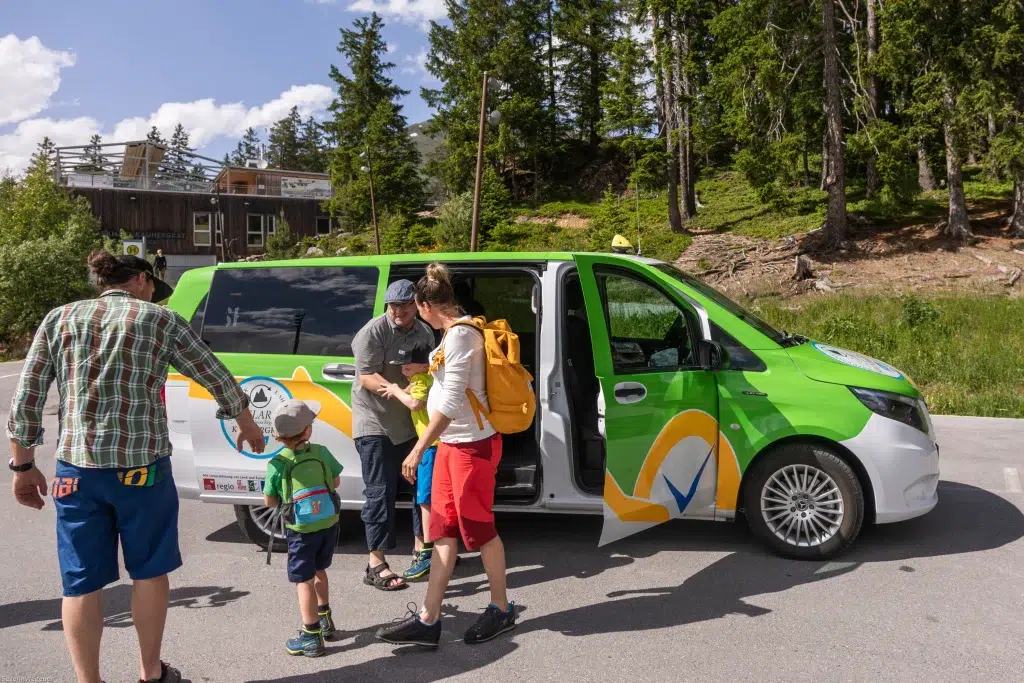 Eine Familie steigt aus einem grün-weißen Lieferwagen aus, um einen nachhaltigen Urlaub in der Nähe eines Waldgebiets zu verbringen.