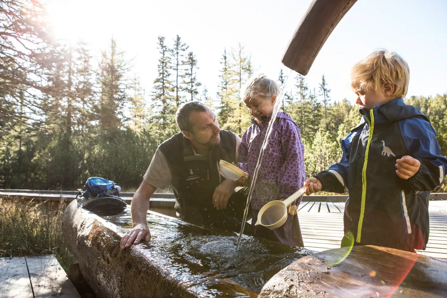 Ein Erwachsener und zwei Kinder sammeln während eines Familienurlaubs im Kaunertal Wasser im Freien.