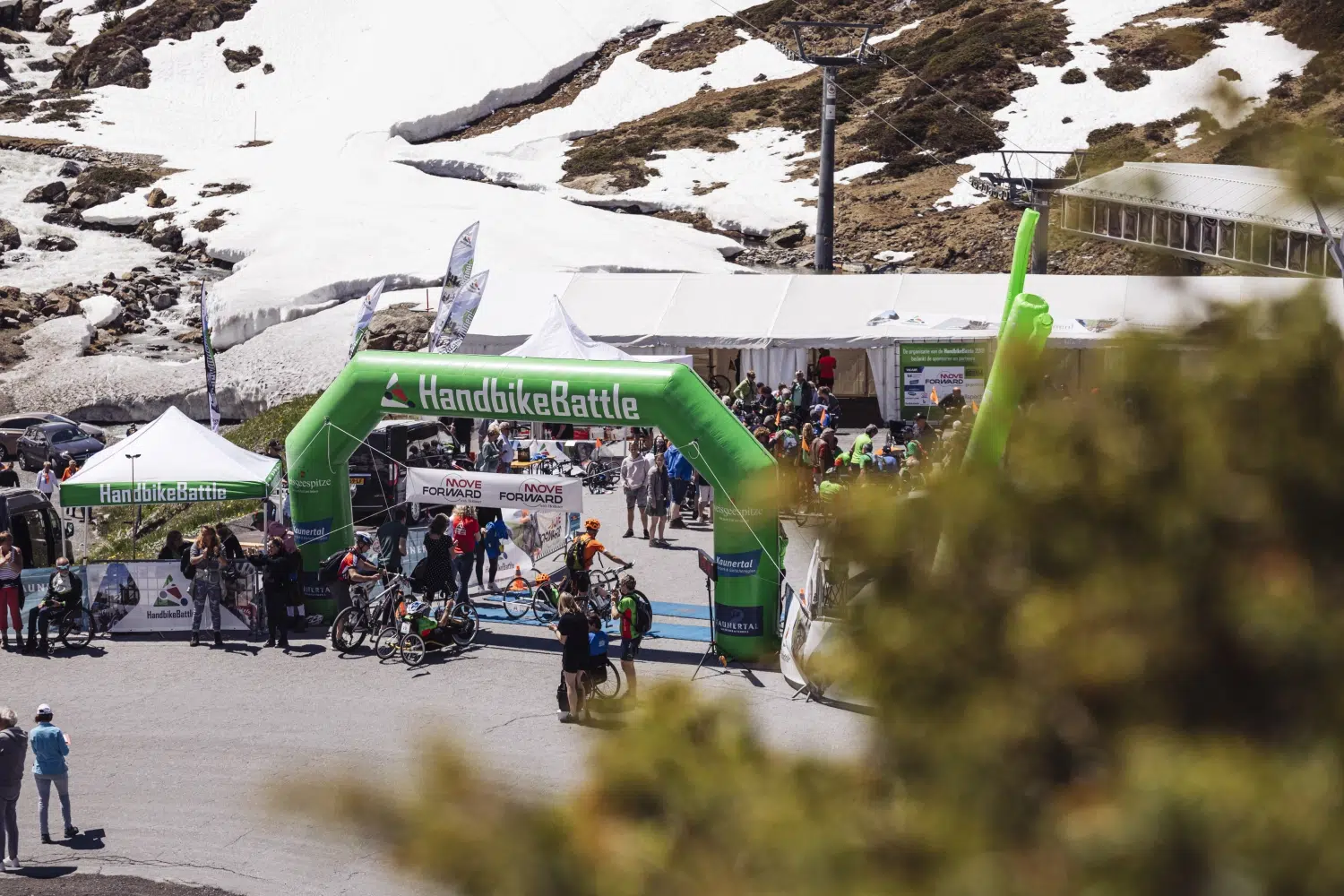 Radfahrer versammeln sich unter einem grünen HandbikeBattle-Bogen bei verschneiten Veranstaltungen im Kaunertal.