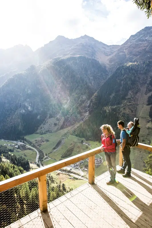 Drei Personen stehen auf einer Holzterrasse im Kaunertaler Sommer und blicken auf ein malerisches Bergtal.